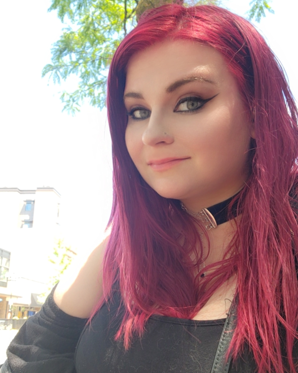 Smiling person with long magenta hair standing outside on a sunny day
