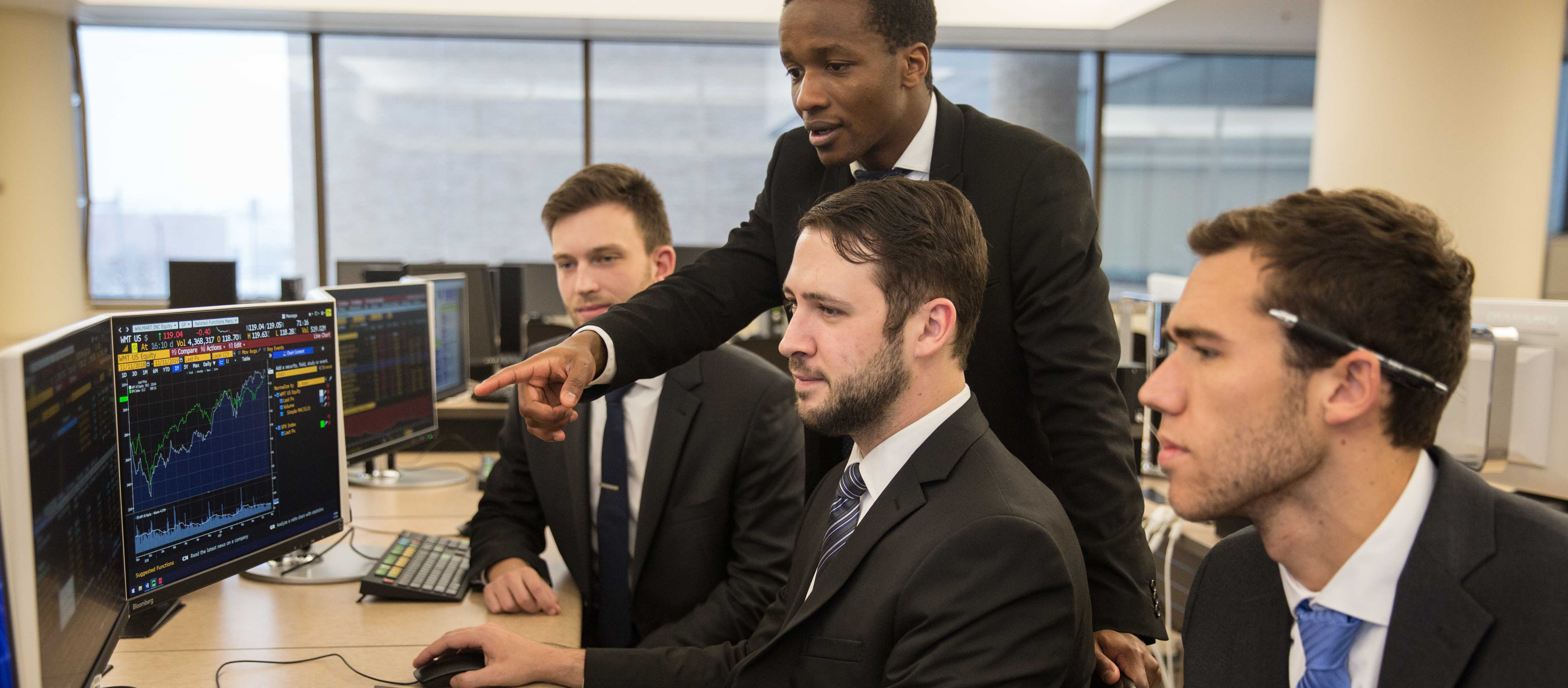 Four male students in suits look at computer screens.